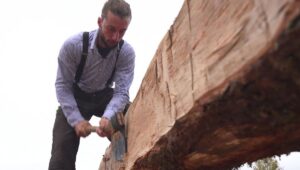 Charpentier travaillant à la hache une pièce de charpente en bois, geste hérité des bâtisseurs nordiques