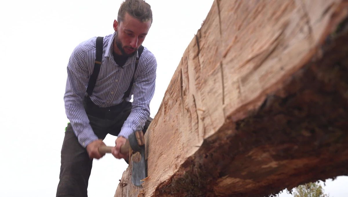 Charpentier travaillant à la hache une pièce de charpente en bois, geste hérité des bâtisseurs nordiques